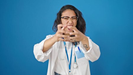 Photo for Young beautiful hispanic woman doctor angry and stressed over isolated blue wall background - Royalty Free Image