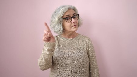 Téléchargez les photos : Femme d'âge moyen aux cheveux gris disant non avec doigt sur fond rose isolé - en image libre de droit