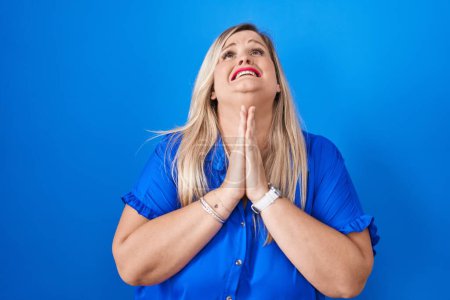 Photo for Caucasian plus size woman standing over blue background begging and praying with hands together with hope expression on face very emotional and worried. begging. - Royalty Free Image
