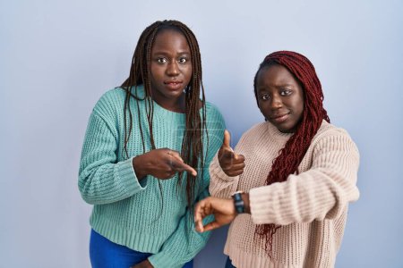 Photo for Two african woman standing over blue background in hurry pointing to watch time, impatience, upset and angry for deadline delay - Royalty Free Image