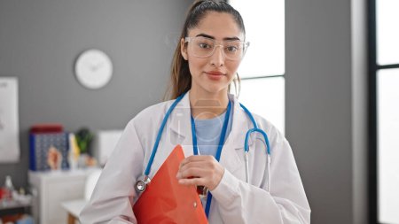 Photo for Young beautiful hispanic woman doctor smiling confident holding medical report at clinic - Royalty Free Image