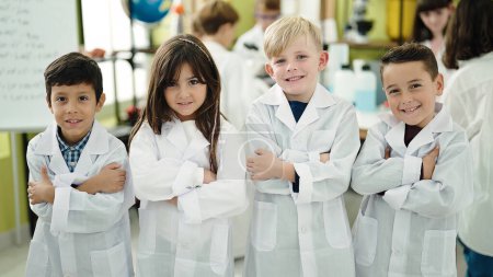 Foto de Grupo de niños científicos estudiantes sonriendo confiados de pie con los brazos cruzados gesto en el aula de laboratorio - Imagen libre de derechos