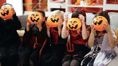 Téléchargez les photos : Groupe d'enfants portant costume d'Halloween couvrant visage avec panier de citrouille à la maison - en image libre de droit