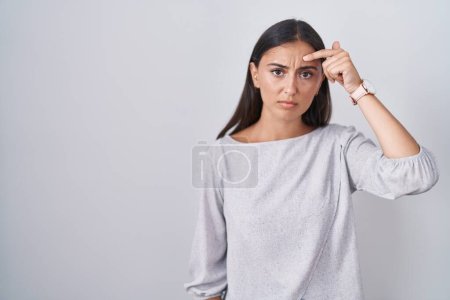Téléchargez les photos : Young hispanic woman standing over white background pointing unhappy to pimple on forehead, ugly infection of blackhead. acne and skin problem - en image libre de droit