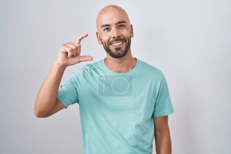 Téléchargez les photos : Homme chauve d'âge moyen debout sur fond blanc geste souriant et confiant avec la main faisant signe de petite taille avec les doigts regardant et la caméra. concept de mesure. - en image libre de droit