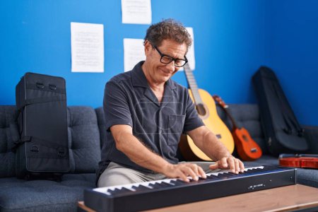 Foto de Hombre de mediana edad músico sonriendo confiado tocando el piano en el estudio de música - Imagen libre de derechos