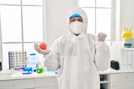 Photo for Hispanic young man working at scientist laboratory holding virus toy screaming proud, celebrating victory and success very excited with raised arms - Royalty Free Image