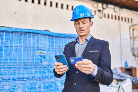 Téléchargez les photos : Jeune homme architecte utilisant smartphone et carte de crédit à la rue - en image libre de droit