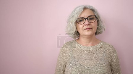 Téléchargez les photos : Middle age woman with grey hair standing with serious expression over isolated pink background - en image libre de droit