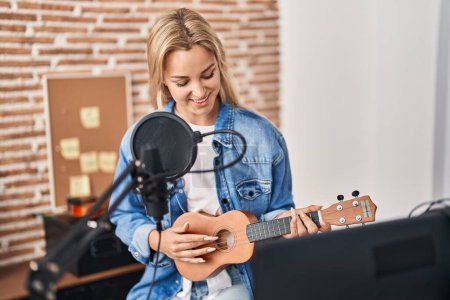 Foto de Joven mujer rubia músico cantando canción tocando ukelele en estudio de música - Imagen libre de derechos
