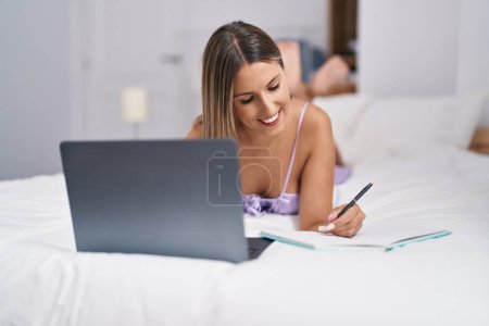 Téléchargez les photos : Jeune belle femme hispanique en utilisant l'écriture d'ordinateur portable sur ordinateur portable dans la chambre - en image libre de droit