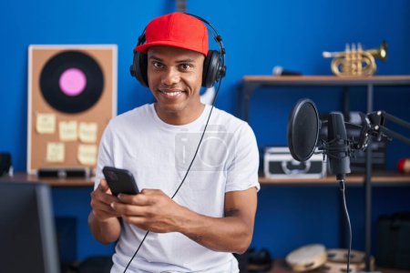 Foto de Joven músico latino sonriendo confiado usando smartphone en estudio de música - Imagen libre de derechos