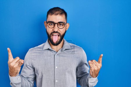 Photo for Middle east man with beard standing over blue background shouting with crazy expression doing rock symbol with hands up. music star. heavy concept. - Royalty Free Image
