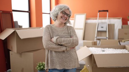 Foto de Mujer de mediana edad con el pelo gris sonriendo confiado de pie con los brazos cruzados gesto en el nuevo hogar - Imagen libre de derechos
