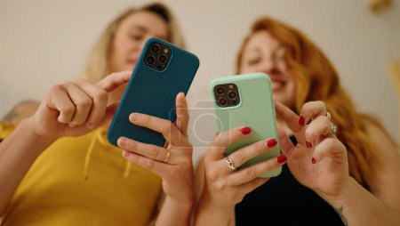 Foto de Dos mujeres usando teléfonos inteligentes de pie en casa - Imagen libre de derechos