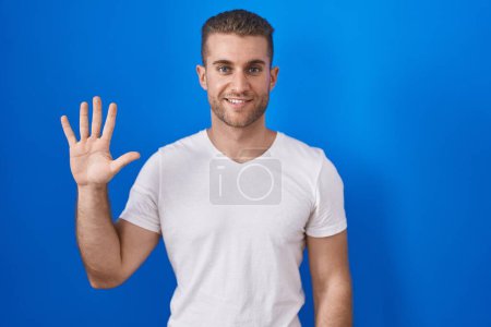 Photo for Young caucasian man standing over blue background showing and pointing up with fingers number five while smiling confident and happy. - Royalty Free Image