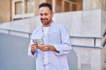 Téléchargez les photos : Jeune homme caucasien souriant confiant compter les dollars à la rue - en image libre de droit