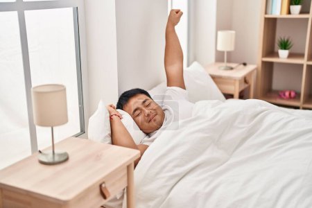 Foto de Joven hombre chino estirando los brazos acostado en la cama en el dormitorio - Imagen libre de derechos