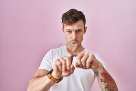 Foto de Caucásico hombre de pie sobre rosa fondo rechazo expresión cruzando dedos haciendo signo negativo - Imagen libre de derechos