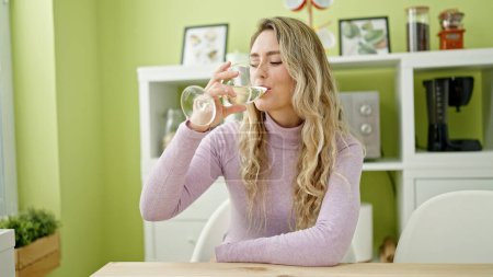 Téléchargez les photos : Jeune femme blonde buvant un verre de vin assis sur la table à manger - en image libre de droit