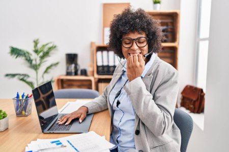 Photo for Black woman with curly hair wearing call center agent headset at the office looking stressed and nervous with hands on mouth biting nails. anxiety problem. - Royalty Free Image
