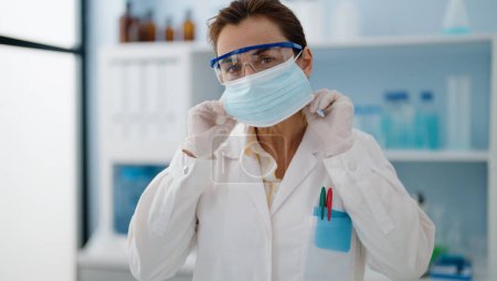 Photo for Middle age hispanic woman wearing scientist uniform and medical mask at laboratory - Royalty Free Image