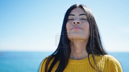 Téléchargez les photos : Jeune belle femme hispanique respirant les yeux fermés au bord de la mer - en image libre de droit