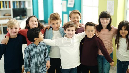 Téléchargez les photos : Groupe d'enfants étudiants souriants confiants se serrant dans leurs bras en classe - en image libre de droit