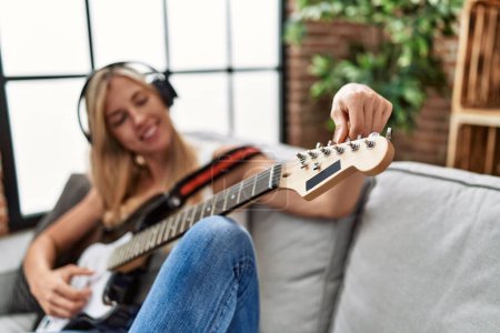 Téléchargez les photos : Jeune femme blonde souriant confiant jouer de la guitare électrique à la maison - en image libre de droit
