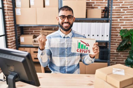 Photo for Middle east man with beard working at small business ecommerce holding crisis banner screaming proud, celebrating victory and success very excited with raised arms - Royalty Free Image