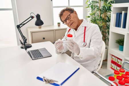 Foto de Hombre de mediana edad vistiendo uniforme médico sosteniendo sonda de orina vacía en la clínica - Imagen libre de derechos