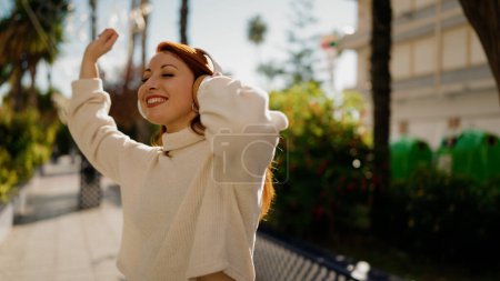 Téléchargez les photos : Jeune rousse femme écouter de la musique et danser au parc - en image libre de droit