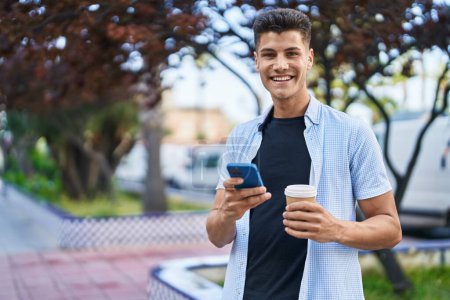 Téléchargez les photos : Jeune homme hispanique utilisant smartphone boire du café au parc - en image libre de droit