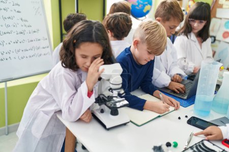 Téléchargez les photos : Groupe d'élèves utilisant un microscope pour écrire sur un carnet de notes dans une salle de classe de laboratoire - en image libre de droit