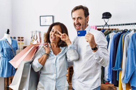 Photo for Hispanic middle age couple holding shopping bags and credit card doing peace symbol with fingers over face, smiling cheerful showing victory - Royalty Free Image