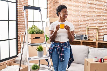 Foto de Mujer afroamericana sonriendo confiada bebiendo café en nuevo hogar - Imagen libre de derechos