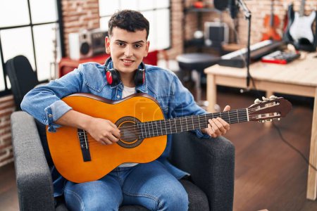 Foto de Joven músico no binario tocando la guitarra clásica en el estudio de música - Imagen libre de derechos