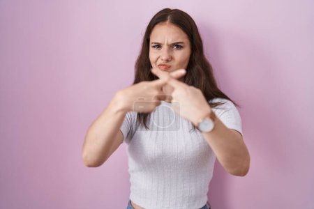 Photo for Young hispanic girl standing over pink background rejection expression crossing fingers doing negative sign - Royalty Free Image