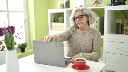 Téléchargez les photos : Middle age woman with grey hair using laptop sitting on table at home - en image libre de droit