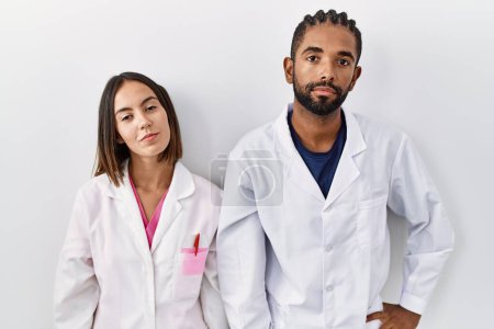 Photo for Young hispanic doctors standing over white background relaxed with serious expression on face. simple and natural looking at the camera. - Royalty Free Image