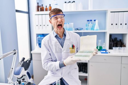 Foto de Hombre caucásico trabajando en laboratorio científico enojado y loco gritando frustrado y furioso, gritando con ira mirando hacia arriba. - Imagen libre de derechos