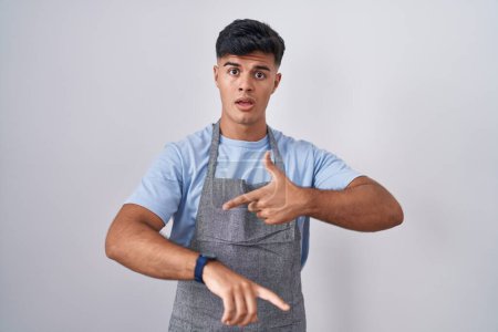 Photo for Hispanic young man wearing apron over white background in hurry pointing to watch time, impatience, upset and angry for deadline delay - Royalty Free Image