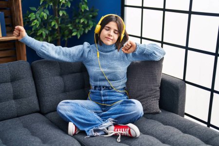 Téléchargez les photos : Jeune belle femme hispanique dansant et écoutant de la musique assise sur le canapé à la maison - en image libre de droit