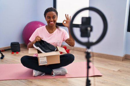Photo for Young african american with braids recording vlog tutorial with smartphone at the gym doing ok sign with fingers, smiling friendly gesturing excellent symbol - Royalty Free Image