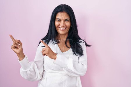 Téléchargez les photos : Femme hispanique mature debout sur fond rose souriant et regardant la caméra pointant avec deux mains et doigts sur le côté. - en image libre de droit