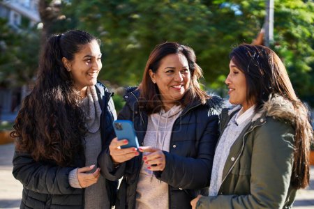 Three woman mother and daughters using smartphone at park-stock-photo