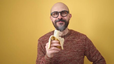 Photo for Young bald man smiling confident holding banana over isolated yellow background - Royalty Free Image