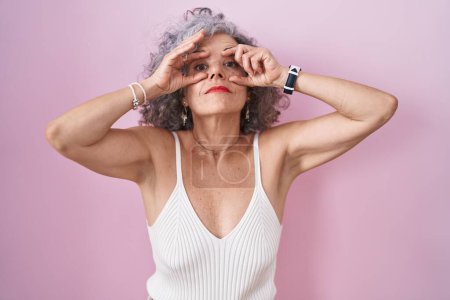 Photo for Middle age woman with grey hair standing over pink background trying to open eyes with fingers, sleepy and tired for morning fatigue - Royalty Free Image
