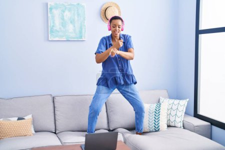 Téléchargez les photos : Femme afro-américaine souriante danse confiante sur le canapé à la maison - en image libre de droit