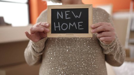 Téléchargez les photos : Middle age woman with grey hair holding blackboard standing at new home - en image libre de droit